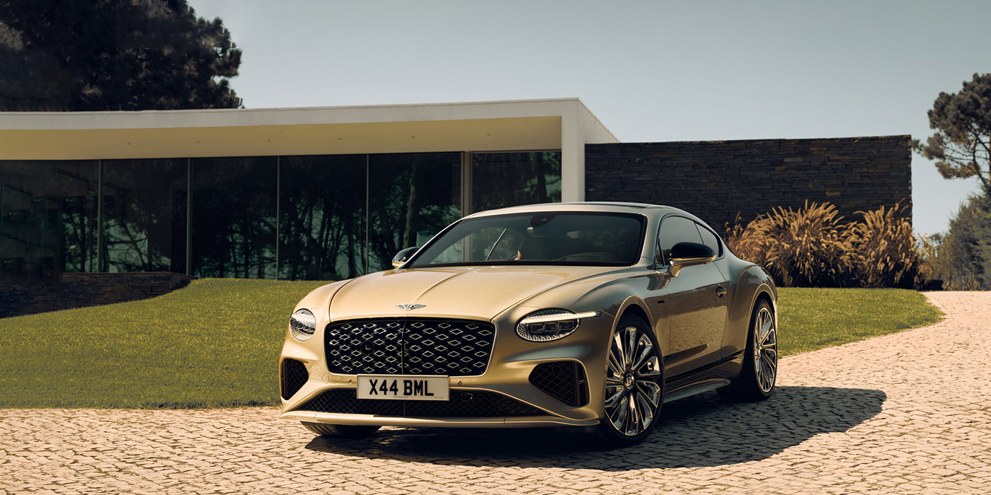 Bentley Jakarta Bentley Continental GT Mulliner coupe front three quarters in Patina paint parked outside a glass fronted building with a grass lawn behind it