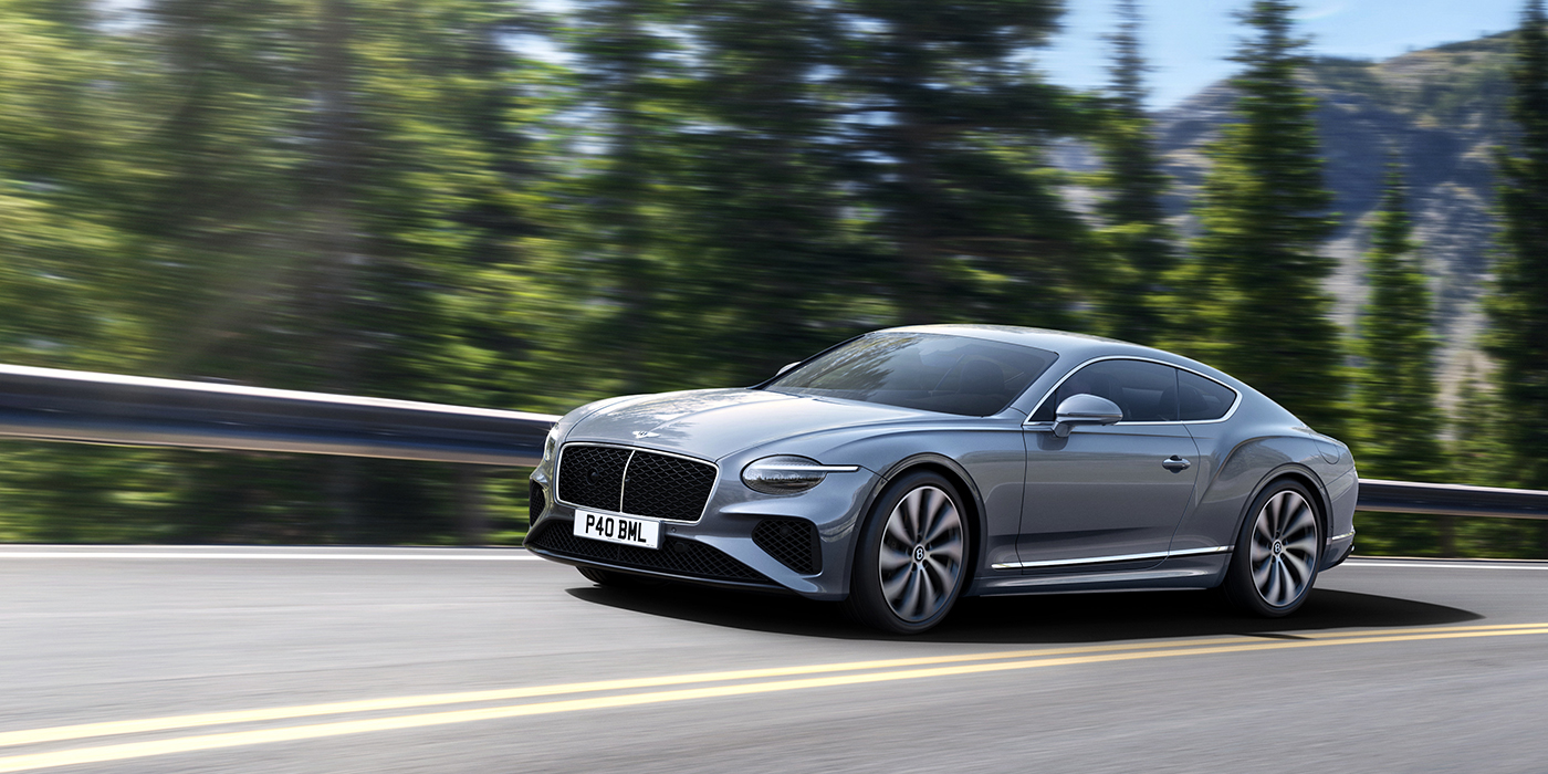 Bentley Jakarta New Bentley Continental GT coupe in Silverlake paint and 22 inch ten-spoke wheels, driving dynamically on a tree-lined road in the sunshine